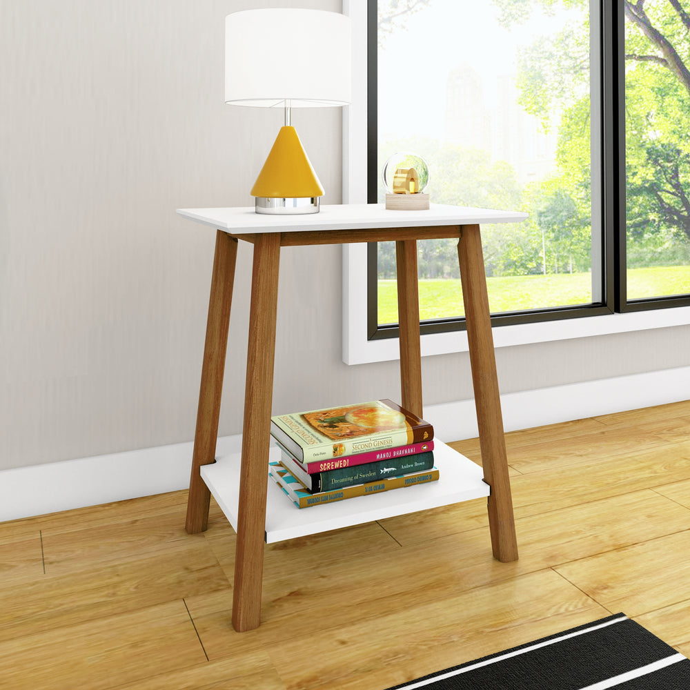 Mid-century modern side table with wooden legs, white top, and lower shelf holding books, placed in a bright living room by a large window.