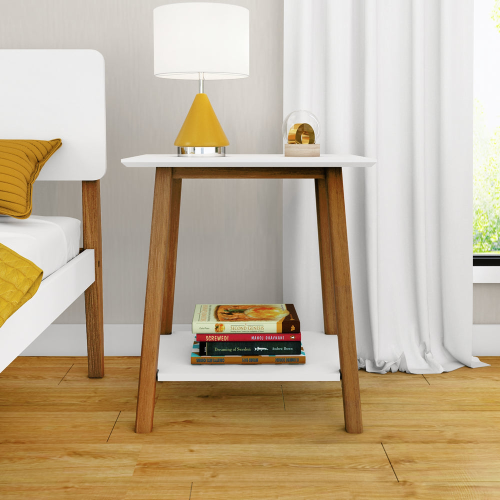 Modern wooden nightstand with a white tabletop and lamp, books neatly stacked below, next to a bed in a cozy bedroom setting.