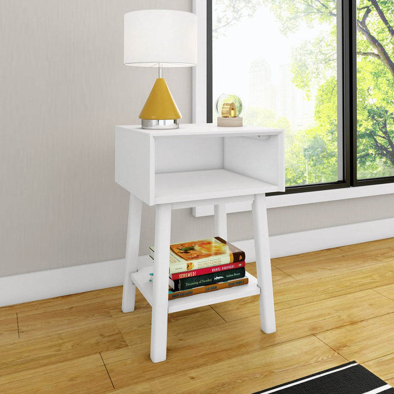 White modern bedside table nightstand with yellow lamp, decorative glass globe and stacked books on lower shelf by sunlit window on hardwood floor