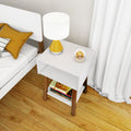 Modern white bedroom nightstand with wooden legs and shelf, yellow bedside table lamp, stacked books on lower shelf, mustard accent pillow and hardwood floor