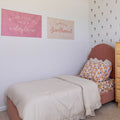 Pink boho girls bedroom with cream comforter, floral sheets and pillow, pink velvet headboard, floral wall decals and inspirational wall banners reading "wildflower" and "girlhood