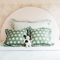 Kids bedroom nursery decor: pale pink rounded upholstered headboard, green sunburst print and striped ruffle pillows, floral wallpaper, plush cow toy