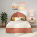 Modern bedroom decor with coral round headboard, neutral striped bedding, yellow accent pillows and blue flower cushion, wooden nightstand with lamp, woven basket fiddle leaf fig, and two framed abstract landscape prints