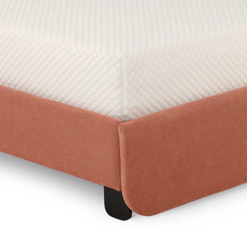 Close-up of quilted white mattress corner on coral textured upholstered bed frame showing fabric detail and black leg