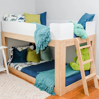 Wooden loft bunk bed with dinosaur-print sheets, teal knitted throw blanket, blue and green pillows and plush dinosaur toys in a styled kids' bedroom
