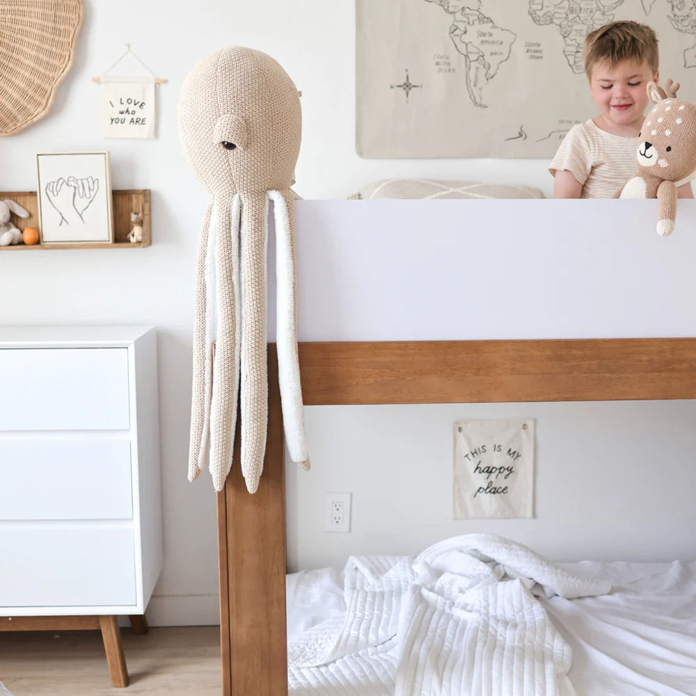Child in cozy bedroom with plush octopus and deer toys on bed, modern decor and wall art.