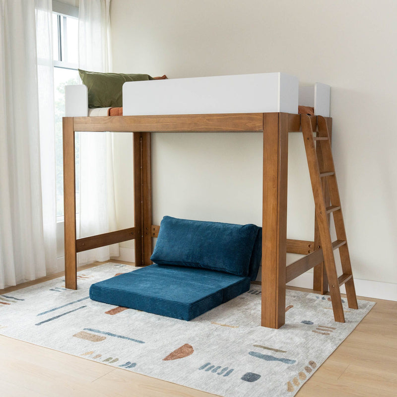 Loft bed with wooden frame featuring a ladder, green pillow on top, and blue cushion seating below, in a bright room with a patterned rug.