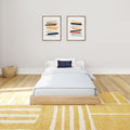 Cozy bedroom interior with modern single bed, abstract wall art, and yellow striped rug.