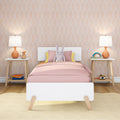 Kids bedroom with pink bedding and plush bunny on a white bed, orange table lamps on wooden nightstands, pastel arch wallpaper and rainbow decor
