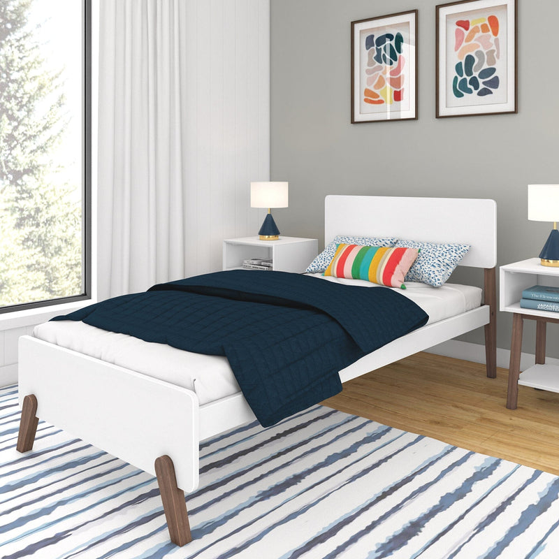 Modern white bedroom with single bed, striped rug, and colorful decor.