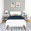 Modern bedroom interior with white platform bed, navy quilt, multicolor striped accent pillow, mid-century nightstands and blue ceramic lamps, abstract framed art on gray wall, and blue-striped area rug