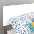 Close-up of modern white rounded headboard with wooden legs and blue spotted leopard-print pillow and bedding