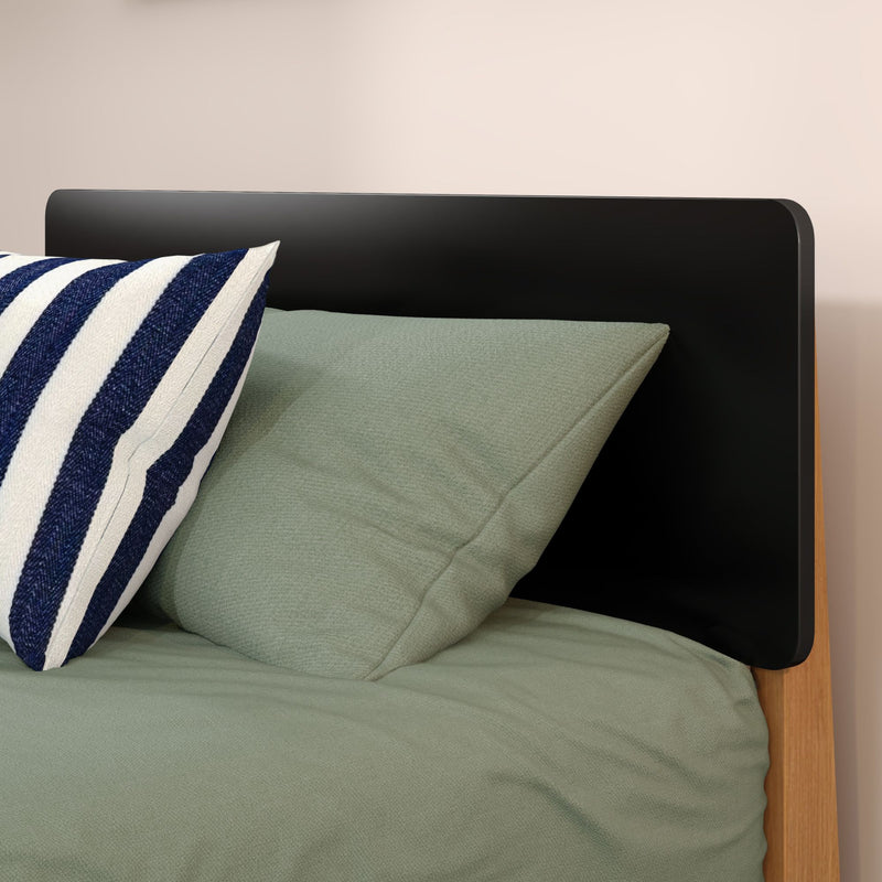 Close-up of modern black headboard with sage green bedding and navy-and-white striped pillow on wooden bed frame, minimalist bedroom decor
