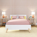 Children's pastel bedroom with pink duvet and pillows, plush bunny on white bed, peach arched wallpaper, orange bedside lamps and wooden nightstands