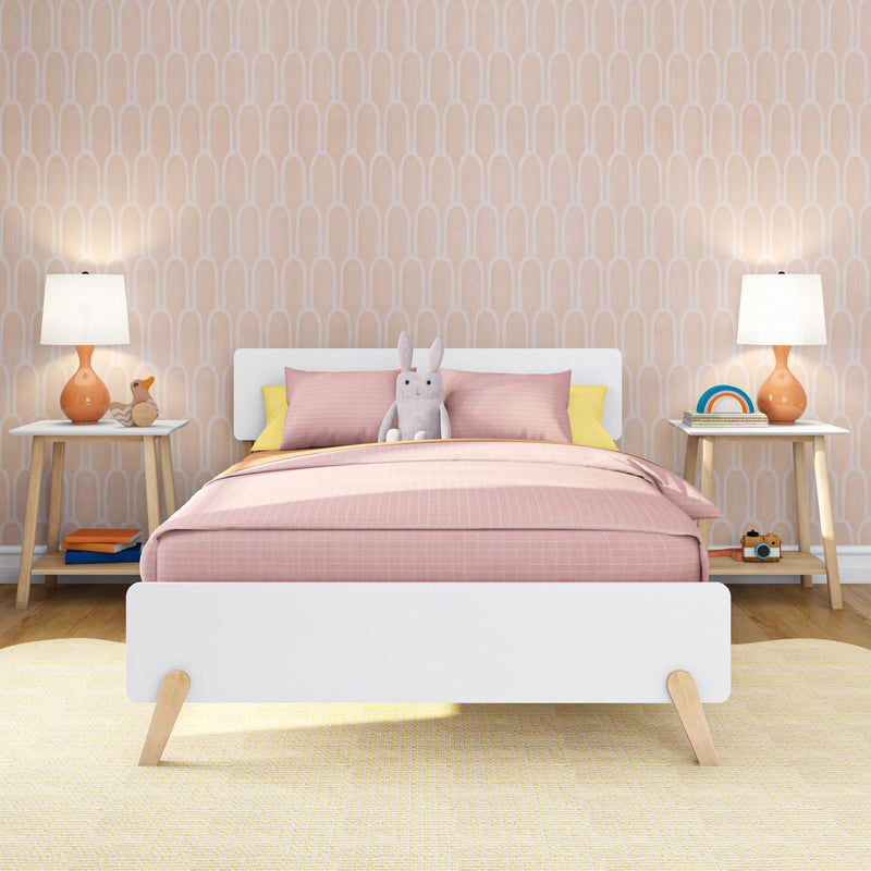Children's pastel bedroom with pink duvet and pillows, plush bunny on white bed, peach arched wallpaper, orange bedside lamps and wooden nightstands