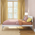 Children's pastel bedroom with pink bedding, mustard-yellow curtains, scalloped area rug, wooden floor, bedside lamp and stuffed bunny