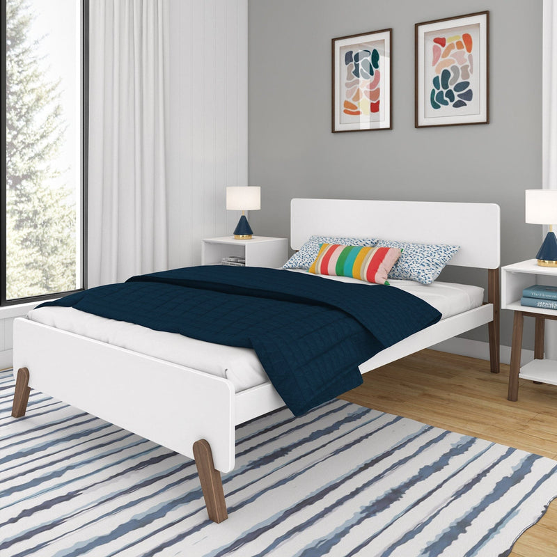 Modern bedroom with a white platform bed, colorful pillows, navy blue comforter, and abstract wall art.