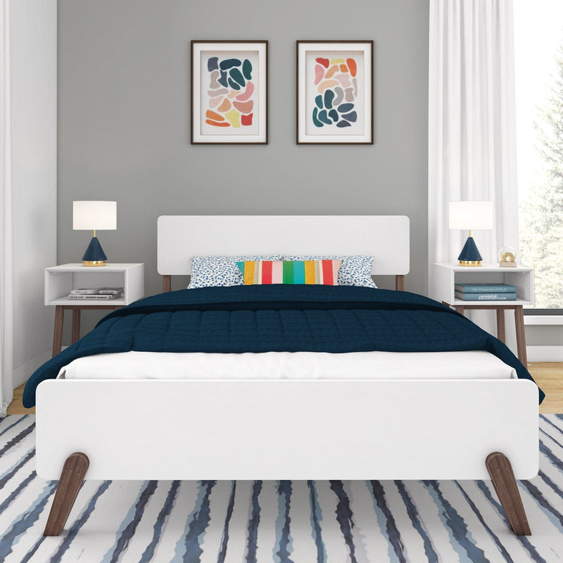 Modern bedroom interior with a sleek white bed frame, navy bedding, colorful pillows, and abstract wall art.