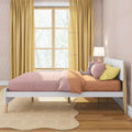 Modern kids bedroom with white platform bed, pink and orange bedding, yellow curtains, plush bunny on pillows, bedside lamp, scalloped rug and large window with tree view