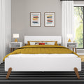 Modern minimalist bedroom with white platform bed, mustard quilted duvet, black-and-white striped rug, mid-century nightstands with lamps, abstract framed wall art and large sunlit window