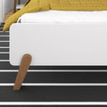Mid-century modern white bed with walnut tapered legs, mustard quilt and black-and-white striped rug in a minimalist bedroom