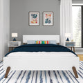 Modern mid-century bedroom with white platform bed, navy quilt, colorful striped accent pillow, matching nightstands and lamps, abstract wall art, gray accent wall, and blue-striped rug by a large window
