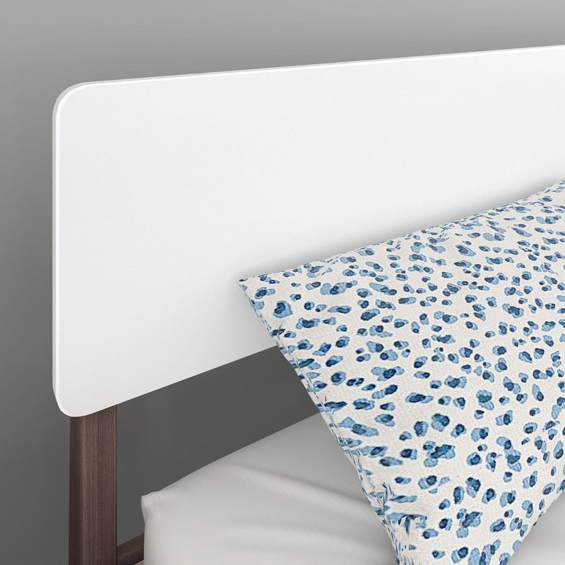 White minimalist headboard with walnut wood legs and blue leopard-print decorative pillow on white bedding, modern bedroom decor