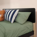 Close-up of green textured bedding with navy-striped pillow, leather teddy bear toy and modern black headboard on wooden bed frame