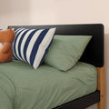 Green textured bedding with navy-striped pillow, tan teddy bear and black headboard on wooden bed frame