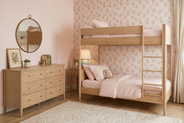 Wooden twin bunk beds in a pink floral kids' bedroom with soft pink bedding, mid-century dresser, round wall mirror, bedside lamp and cozy rug — kids' room decor and small-space bunk bed ideas.