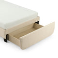 Beige upholstered storage bed with open under-bed pull-out wooden drawer and white textured mattress corner close-up