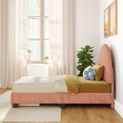 Sunlit modern bedroom decor with a pink upholstered twin bed, mustard bedding and blue flower pillow, sheer curtains, fiddle‑leaf fig plant, framed abstract art, and light wood floor