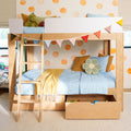 Wooden loft bunk bed with light blue bedding, yellow throw, flower cushion, stuffed toy and under-bed storage drawers, decorated with colorful bunting and orange polka-dot wall in a kids' bedroom