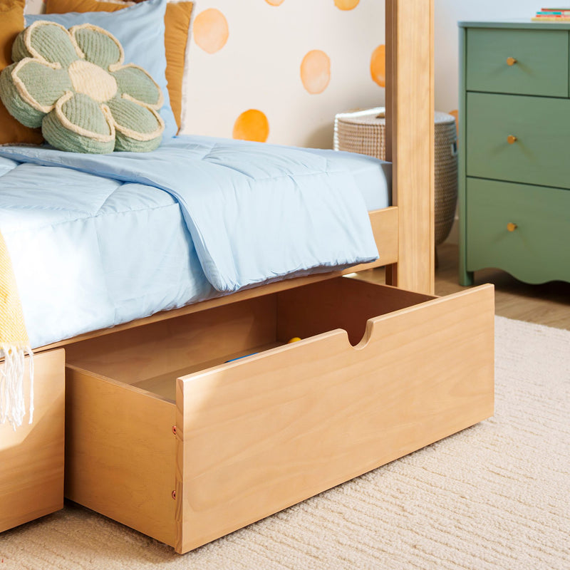 Wooden twin kids bed with light blue comforter, green flower-shaped pillow and pull-out underbed storage drawers in a children's bedroom with green dresser