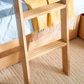 Close-up of a light natural wood bunk bed ladder with slatted rungs beside blue bedding and a yellow fringed throw, modern bedroom decor