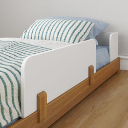 Child's bed with safety rail, wooden frame, and striped bedding in a modern bedroom.