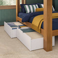 Wooden four-poster bed with navy bedding, green-and-white striped pillows and mustard throw, two white underbed storage drawers pulled out on carpet