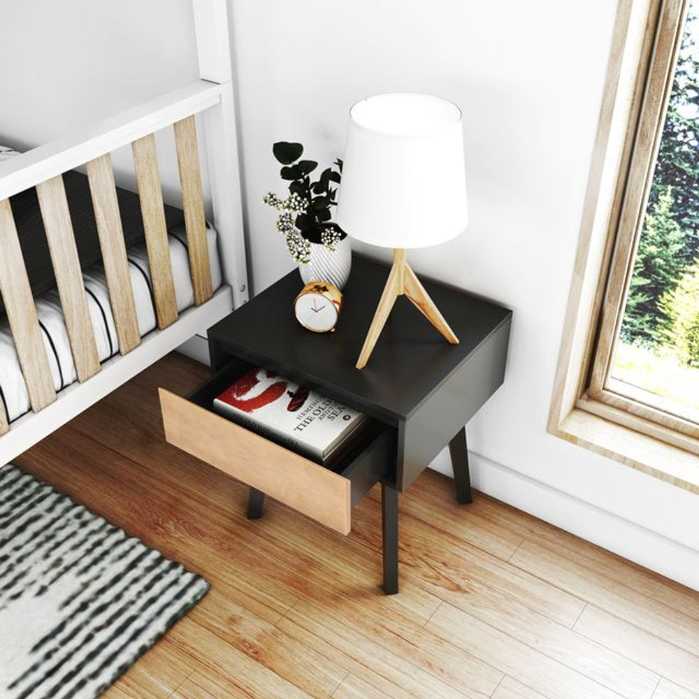 Modern bedside table with open drawer, table lamp, clock, and decorative plant in a stylish bedroom setting.