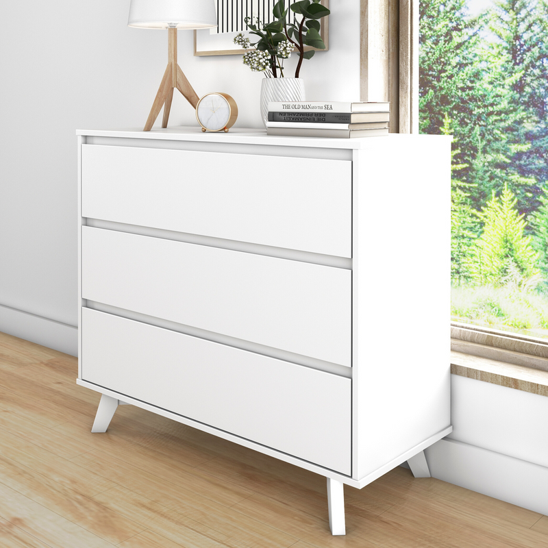 Modern white dresser with three drawers in a bright, minimalist bedroom setting featuring a wooden floor and large window with greenery outside.