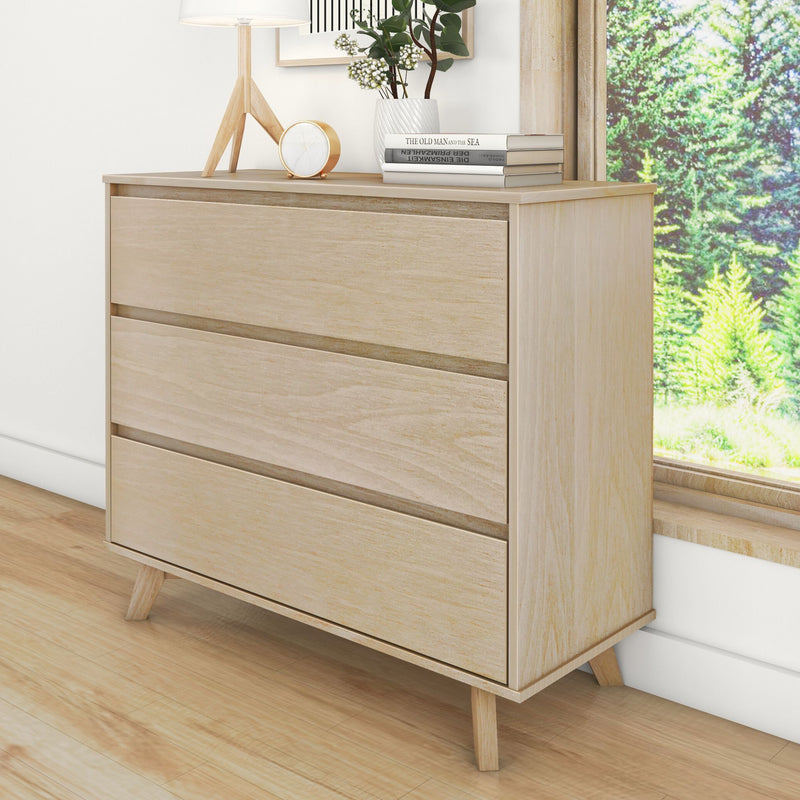 Light oak three-drawer dresser with mid-century modern legs — minimalist bedroom storage chest styled with lamp, clock, books, and vase by a sunny window