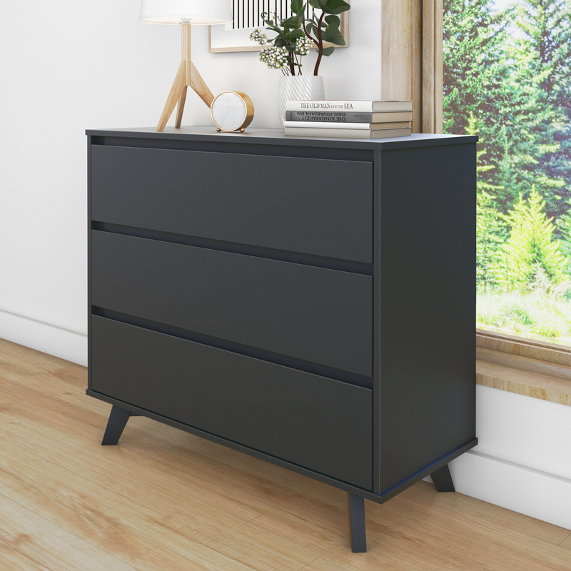 Black modern dresser with three drawers and wooden legs next to window, featuring decorative items on top, in a bright room with hardwood floors.
