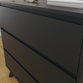 Close-up of a modern matte black 3-drawer dresser with recessed handles on hardwood floor, minimalist bedroom storage with books and a small clock on top