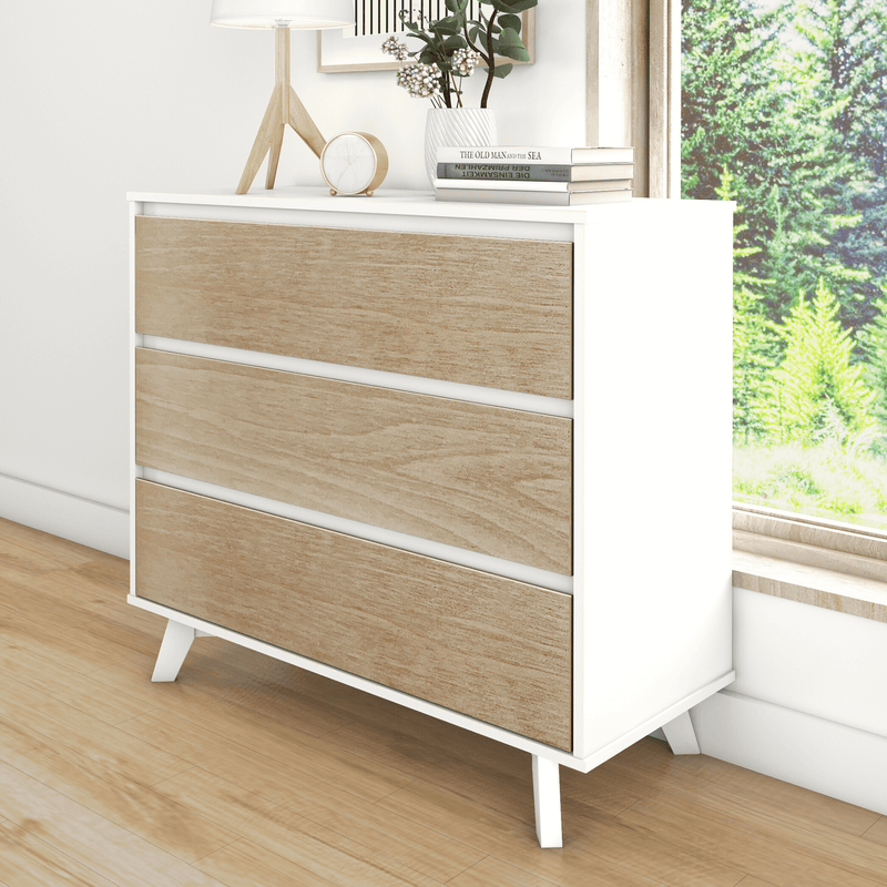 Modern white dresser with light wood three drawers and mid-century legs, styled with lamp, clock and books by a sunny window