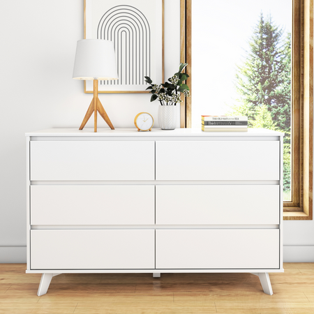 White six-drawer dresser in modern bedroom with lamp, clock, and books, next to large window.