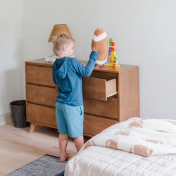 Child organizing toys on a wooden dresser in a bright modern bedroom with a plush football and colorful stacking blocks.