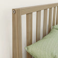 Close-up of a modern light oak slatted wooden headboard with vertical slats and green bedding in a minimalist bedroom