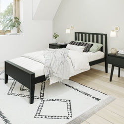 Modern minimalist bedroom with a black wooden bed frame, white bedding and throw, geometric black-and-white rug, matching black nightstands, wall sconces, light wood floor and potted plant by the window
