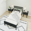 Modern minimalist Scandinavian bedroom with black wooden bed, matching nightstands, wall sconces, soft green pillows and patterned rug on light hardwood floor