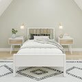 Minimalist Scandinavian bedroom with white platform bed, slatted wood headboard, green accent pillows, matching nightstands, wall sconces and black-and-white patterned rug