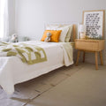 Cozy neutral kids bedroom with white toddler bed, green check bedding, orange pom-pom pillow, stuffed animals, wooden nightstand, lamp and framed typographic wall art
